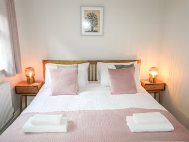 A bedroom with a wooden bed with white and pink bedding with two bedside tables with lamps at 3 Trem Y Dolydd in Dolgarrog near Llanrwst