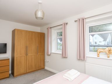 A bedroom with wooden wardrobe and chest of drawers pink curtains and a bed with folded towels at 3 Trem Y Dolydd Dolgarrog near Llanrwst