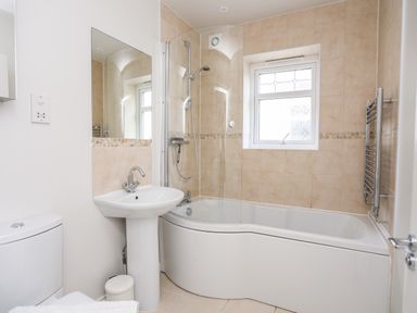 A bathroom with a bathtub shower combo, pedestal sink, toilet, and a window at 3 Trem Y Dolydd in Dolgarrog near Llanrwst