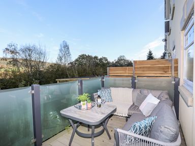A balcony with a corner sofa table and plants overlooking trees at 3 Trem Y Dolydd in Dolgarrog near Llanrwst
