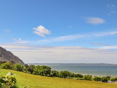 A grassy field with trees and a body of water under a partly cloudy sky at 3 Trem Y Dolydd in Dolgarrog near Llanrwst