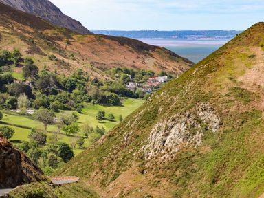 A valley with trees houses green fields and hills with a body of water in the background at 3 Trem Y Dolydd Dolgarrog near Llanrwst