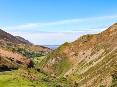 A valley with hills on both sides and a road on the left with some people riding bicycles at 3 Trem Y Dolydd Dolgarrog near Llanrwst
