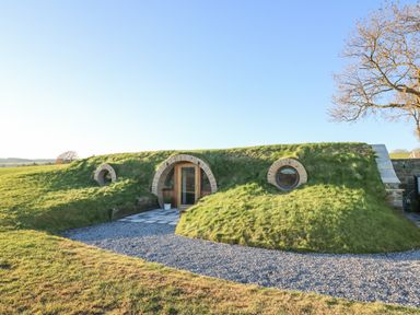 A small earth house with a grass roof and circular windows at Tan y Wawr- Onnen in Llanfair Caereinion