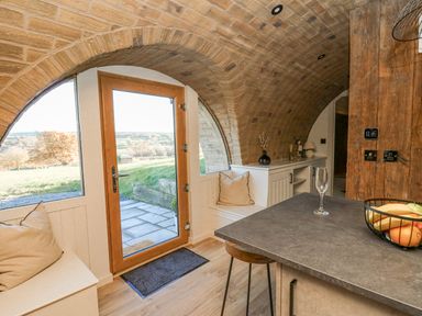 A kitchen area with a stone countertop, two stools, pillows on built-in benches, and arched brick ceiling at Tan y Wawr- Onnen in Llanfair Caereinion