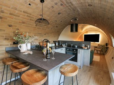 A kitchen with a curved brick ceiling wooden stools and a living area with a TV at Tan y Wawr Onnen Llanfair Caereinion