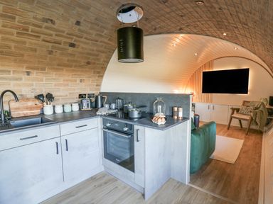 A kitchen area with oven sink and utensils connected to a living room with a sofa TV and chair at Tan y Wawr- Onnen in Llanfair Caereinion