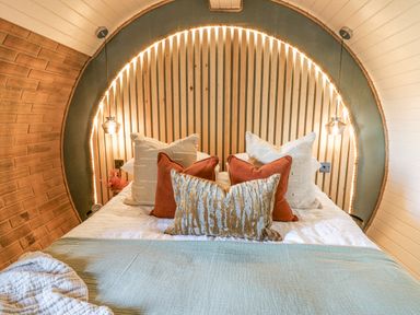 A bed with multiple pillows and a blanket inside a curved wooden room at Tan y Wawr- Onnen in Llanfair Caereinion