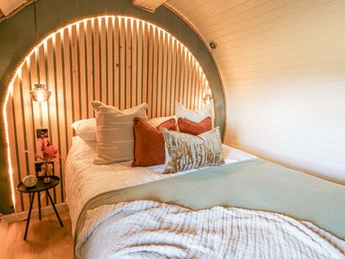 A bedroom with a bed with multiple pillows beside a round spark with lights and a small table with a flower in a vase at Tan y Wawr- Onnen in Llanfair Caereinion
