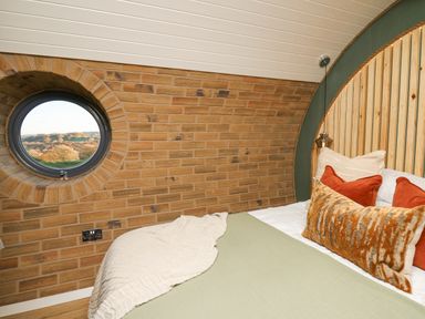A bedroom with a bed, decorative pillows, a round window, and brick walls at Tan y Wawr- Onnen in Llanfair Caereinion