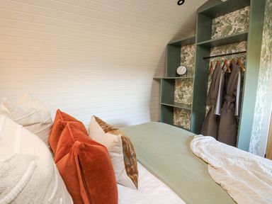 A bedroom with pillows on the bed and an open closet with robes at Tan y Wawr- Onnen in Llanfair Caereinion