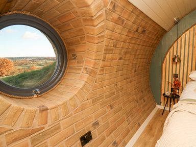 A bedroom with a round window brick walls wooden floor and a bedside table at Tan y Wawr- Onnen in Llanfair Caereinion