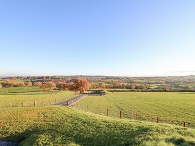 A rural landscape with green fields a fenced dirt path and trees at Tan y Wawr Onnen in Llanfair Caereinion