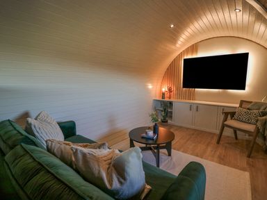 A living room with a green sofa white pillows a round black coffee table a wooden chair and a wall mounted television at Tan y Wawr- Onnen in Llanfair Caereinion
