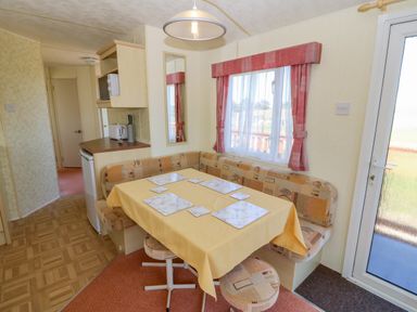 A dining area with a table covered by a yellow tablecloth and seating in a caravan at Gorphwysfa Caravan Tregele near Cemaes Bay