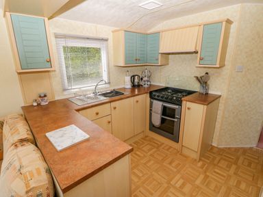 A kitchen with wood cabinets and green cupboard doors a gas stove a sink next to a window and a countertop at Gorphwysfa Caravan in Tregele near Cemaes Bay