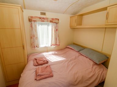 A bedroom with a double bed with pink bedding and towels and built in wooden cabinets at Gorphwysfa Caravan Tregele near Cemaes Bay
