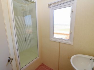 A bathroom with a shower enclosure a window and a sink at Gorphwysfa Caravan Tregele near Cemaes Bay
