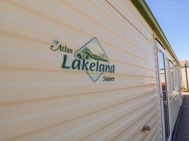 Exterior side view of a beige caravan with Atlas Lakeland Super branding and multiple windows on a wooden deck at Gorphwysfa Caravan in Tregele near Cemaes Bay