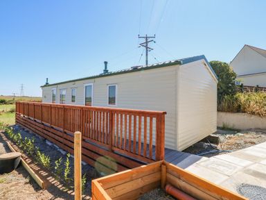 A mobile home with a wooden railing and plants in a garden at Gorphwysfa Caravan in Tregele near Cemaes Bay