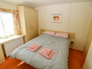 A bedroom with a double bed two pink towels wardrobe desk and window at Gorphwysfa Caravan Tregele near Cemaes Bay