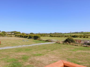A grassy field with a gravel path and two chairs with a table in the distance at Gorphwysfa Caravan in Tregele near Cemaes Bay