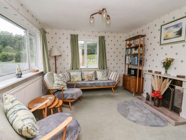 A sitting room with wooden furniture green curtains a fireplace and a bookshelf at Llwynon in Goginan near Aberystwyth