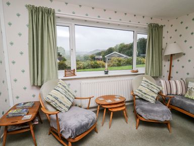 A sitting room with two wooden armchairs cushions side table and lamp by a window at Llwynon in Goginan near Aberystwyth