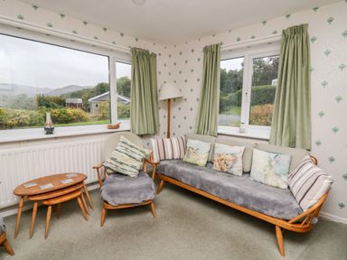 A corner seating area with a sofa and armchair with cushions and nesting wooden tables at Llwynon in Goginan near Aberystwyth