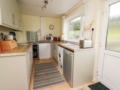 A narrow kitchen with wooden countertops washing machine microwave and toaster at Llwynon in Goginan near Aberystwyth