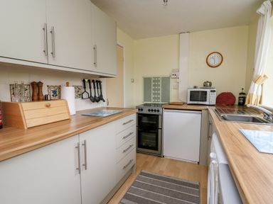 A kitchen with wooden countertops white cabinets a stove microwave and a sink at Llwynon in Goginan near Aberystwyth