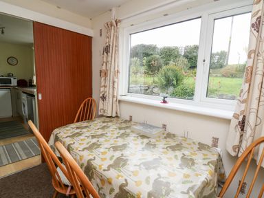A dining area with a table covered in a bird patterned cloth and wooden chairs next to a window at Llwynon in Goginan near Aberystwyth