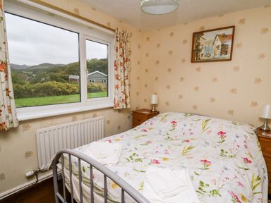 A bedroom with a double bed with floral bedding two bedside tables with lamps a window with floral curtains and a wall painting at Llwynon in Goginan near Aberystwyth