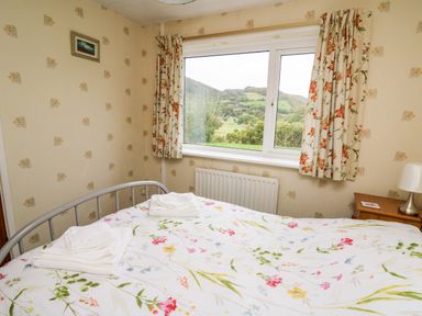 A bedroom with a bed and floral bedding near a window showing a landscape at Llwynon in Goginan near Aberystwyth