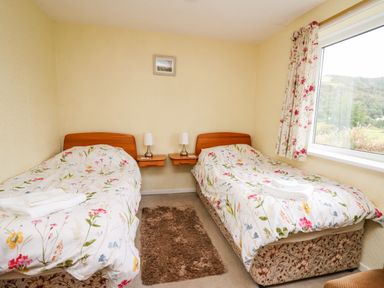A bedroom with two single beds with floral bedding and a window showing a landscape at Llwynon in Goginan near Aberystwyth