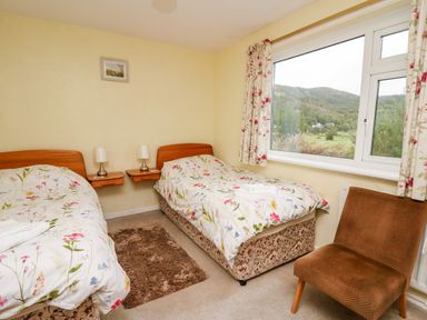 A bedroom with two single beds a brown chair a window with floral curtains and a landscape view at Llwynon in Goginan near Aberystwyth