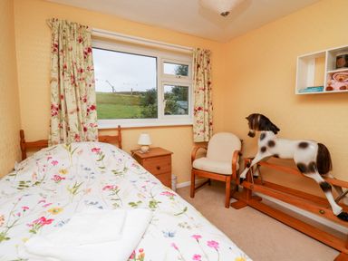 A bedroom with a single bed floral curtains a rocking horse and an armchair at Llwynon Goginan near Aberystwyth