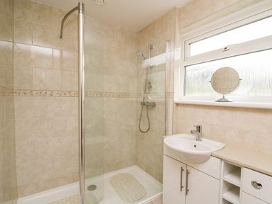 A bathroom with a shower area a sink and a window with a round mirror on the sill at Llwynon in Goginan near Aberystwyth