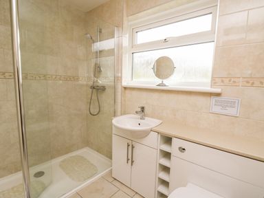 A bathroom with a shower area a small sink with cabinet and a countertop under a window at Llwynon in Goginan near Aberystwyth