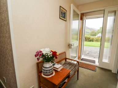 An entryway with a wooden bench holding a vase of flowers and books next to an open door showing an outdoor view at Llwynon in Goginan near Aberystwyth