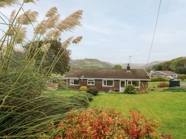 A single-story brick house with a tiled roof surrounded by grass and plants in a rural landscape at Llwynon in Goginan near Aberystwyth