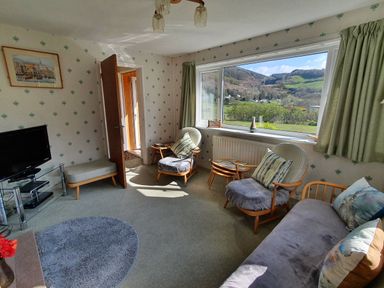 A living room with chairs and a sofa near a large window overlooking hills at Llwynon in Goginan near Aberystwyth