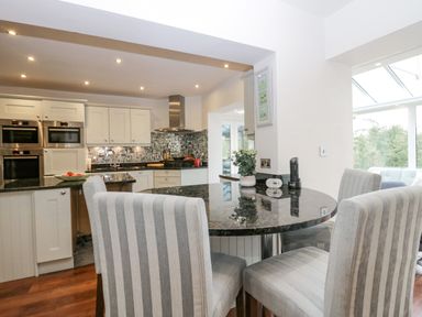 A kitchen with white cabinets black countertops striped dining chairs and a round table at Holme Fell in Coniston
