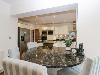 A kitchen with stainless steel refrigerator and double oven a round dining table with striped chairs and a flower vase at Holme Fell in Coniston