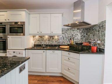 A kitchen with white cabinets black countertops mosaic tile backsplash and stainless steel appliances at Holme Fell in Coniston