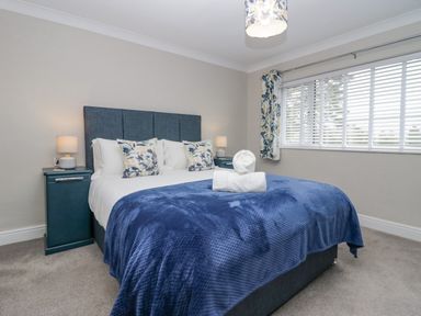 A bedroom with a bed covered by blue bedding and floral pillows with two side tables and lamps by a window at Holme Fell in Coniston