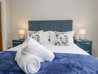 A bedroom with a bed with blue headboard and two pillows with bedside tables and lamps at Holme Fell in Coniston