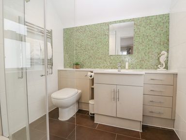 A bathroom with a toilet sink cabinets green tile backsplash and a glass shower enclosure at Holme Fell in Coniston