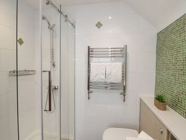 A bathroom with a glass shower enclosure a chrome towel rack with white towels a toilet and green mosaic tile wall at Holme Fell Coniston