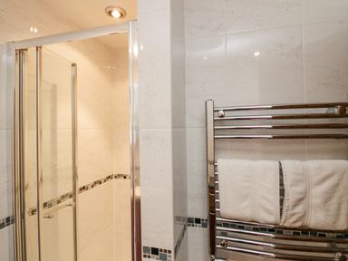 A bathroom with a glass shower enclosure and a towel rack with white towels at Holme Fell in Coniston